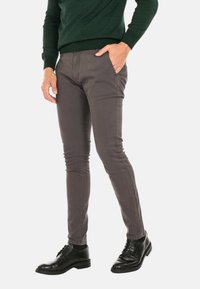 Pantaloni slim-fit grigi realizzati in misto cotone, con una texture liscia e una leggera elasticità. Indossati con scarpe in pelle nere.