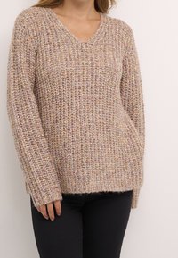 Pull en laine de couleur beige atténué avec un ribbing texturé. Il présente un col en V, des manches longues et une coupe décontractée, avec des fils multicolores subtils.
