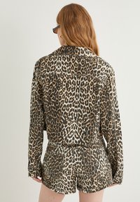 Leopardprint denimskjorte med lange ærmer og cropped design, parret med matchende shorts. Farvepaletten inkluderer sorte, brune og cremefarvede nuancer.