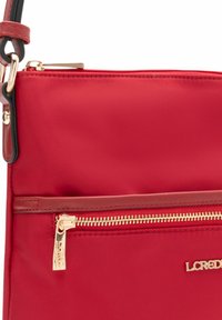 Rote Nylon-Umhängetasche mit goldfarbenen Beschlägen, ausgestattet mit einer vorderen Reißverschlusstasche und einem Logo-Akzent. Glatte Textur, verstellbarer Riemen.