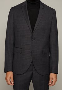 Mörkt rutigt blazer med en slät yta, enkel knappknäppning och två framfickor, bärs över en svart polotröja.