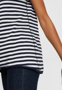 Maglietta a righe blu navy e bianca con orlo arrotondato, maniche corte e dettagli di cucitura visibili, abbinata a jeans in denim scuro.