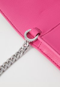 Rosa lærveske med hjørne og en sølvkjede lås. Har glatt tekstur og kontraststing. Utsmykket med en rund metallring.