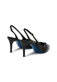 Tacchi alti slingback in pelle nera con punta affusolata, cinturini con fibbia dorata e suole blu, mostrati da dietro su sfondo bianco.
