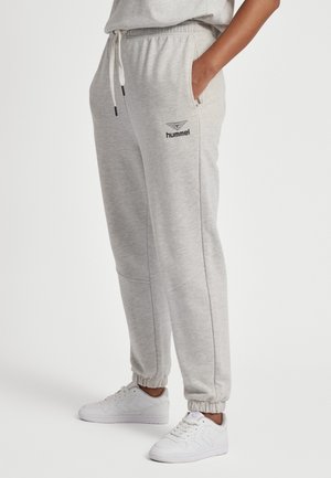 Persoon die lichtgrijze Hummel-sweatpants met elastische boorden en witte sneakers draagt, staand met één hand in de zak tegen een witte achtergrond.