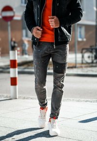 Musta farkkutakki, oranssi collegepaita, kuluneet harmaat farkut, joissa on maalitahroja, ja valkoiset korkeat lenkkarit punaisilla yksityiskohdilla.