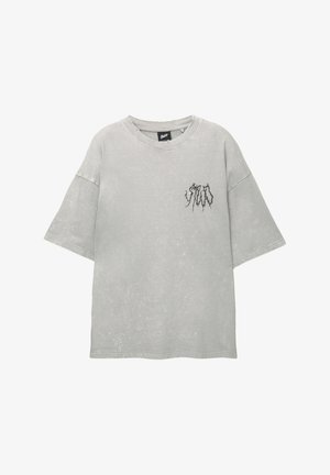Übergrößes graues T-Shirt aus weicher Baumwolle mit einem gebrauchten Finish. Es hat einen runden Ausschnitt und ein kleines schwarzes Grafikdesign auf der Brust.