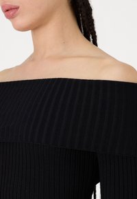 Top preto canelado sem alças com um design ajustado, apresentando linhas verticais e uma textura suave, enfatizando os contornos do corpo.