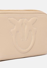 Portafoglio in pelle beige con design impresso che presenta due uccelli. Chiusura lampo dorata e dettagli di cucitura bianca lungo i bordi. Forma compatta e rettangolare.
