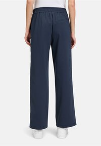 Pantaloni da tuta larghi blu navy con vita elastica e tasca posteriore, realizzati in un tessuto morbido e resistente con una texture liscia.