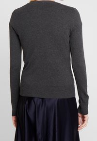 Szary sweter z dzianiny z długimi rękawami, prążkowanym dekoltem i wykończeniem, dopasowany krój, zestawiony z ciemną, satynową spódnicą. Gładka faktura i prosty styl.