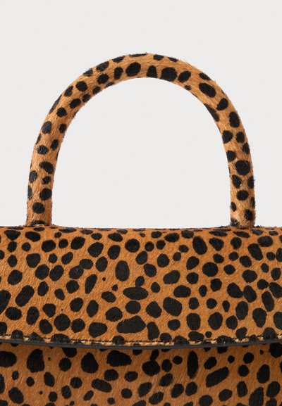 Sac à main imprimé léopard avec poignée arrondie et taches noires sur une surface texturée type fourrure marron.