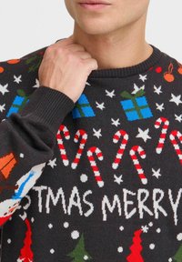 Suéter oscuro con patrones de punto de bastones de caramelo, árboles de Navidad, regalos y copos de nieve. Cuello y puños acanalados.