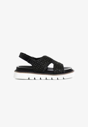 Mustat kudotut slingback-sandaalit, joissa on leikkauksia, teksturoitu päällinen ja paksu valkoinen pohja. Varustettu kiiltävällä mustalla pinnalla ja säädettävällä hihnalla.