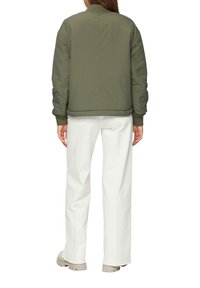 Olijfgroene bomberjack met ribgebreide manchetten en onderrand, met een doorgestikt textuur. Gecombineerd met witte wijde broek en beige laarzen.