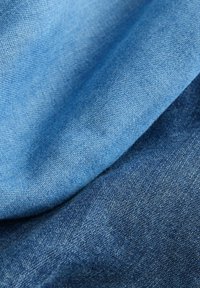 Denim tkanina u svijetlim i tamnim plavim nijansama, koja prikazuje strukturirani tkanje s preklopljenim slojevima, demonstrira različite tonove i mekoću.