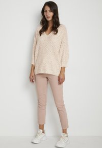 Maglione lavorato a maglia rosa chiaro con scollatura a V, motivo testurizzato e maniche larghe, abbinato a pantaloni attillati rosa chiaro e sneakers bianche.