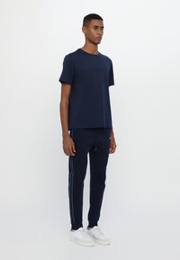 Marineblå bomull T-skjorte med preget logo, kombinert med marineblå joggebukser med hvite sidestriper og hvite joggesko. Enkel design, avslappet passform.