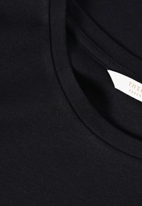 Czarny bawełniany t-shirt z okrągłym dekoltem, o gładkiej fakturze, z metką przyszytą wewnątrz kołnierza z widoczną nazwą marki.