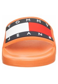 Sandale orange à enfiler avec le logo Tommy Jeans noir, blanc et rouge sur la bride.