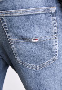 Blå denimjeans med en bakficka som har en liten logotag. Tyget har en slät textur och subtila blek effekter.