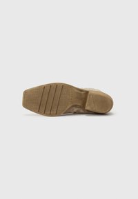 Sole di scarpa in suede marrone con un motivo testurizzato, caratterizzata da una suola di gomma beige e un dettaglio di marchio laterale. Finitura liscia e forma arrotondata.