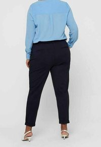 Person wearing a light blue long-sleeve shirt and black tapered pants with white heeled sandals, standing facing away.