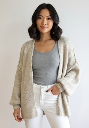 Beżowy dziergany kardigan z szerokimi rękawami, otwartym przodem i miękką fakturą, w połączeniu z szarym, dopasowanym topem na ramiączkach oraz białymi, wysokim stanem jeansami.