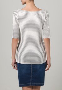 Gestreiftes weißes und marineblaues Oberteil mit Dreiviertelärmeln, das über einen U-Boot-Ausschnitt verfügt und mit einem dunklen Jeans-Bleistiftrock kombiniert wird.