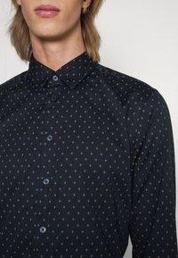 Námořnická košile s knoflíky, s geometrickým zlatým diamantovým vzorem, má klasický límec, dlouhé rukávy a kontrastní knoflíky.