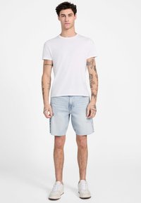 T-shirt en coton blanc à manches courtes, associé à un short en denim bleu clair avec un ourlet effiloché et une coupe décontractée. Porté avec des baskets blanches.