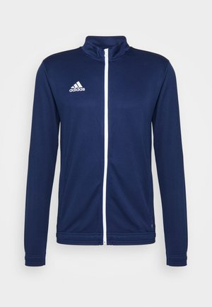 Marineblauwe sportjack gemaakt van gladde stof, met een witte rits, hoge kraag en een geborduurd wit Adidas-logo op de borst.