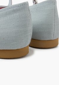Zapatos de tela azul claro con un acabado texturizado, punta redonda y una suela de goma marrón clara baja. Presentan un diseño minimalista con acentos de costura.