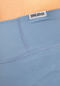 Lichtblauwe sportieve shorts gemaakt van rekbaar materiaal, met platlocknaden en een zichtbaar merklabel met de tekst "SMILODOX."