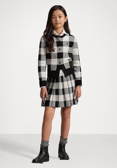 Cardigan lavorato a maglia a quadri bianco e nero con bottoni, abbinato a una gonna plissettata. Stivaletti neri alla caviglia con calze texturizzate.