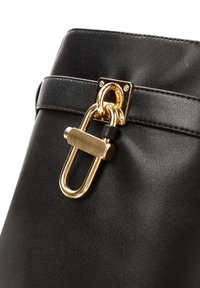 Sac à main en cuir noir avec des détails en métal doré, une attache rectangulaire et une texture lisse avec des accents de couture.