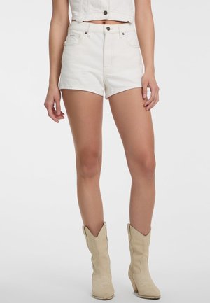 Shorts en denim blanc avec une taille haute, des ourlets retroussés et des poches avant. Associés à des bottes de cowboy beiges avec des coutures décoratives.