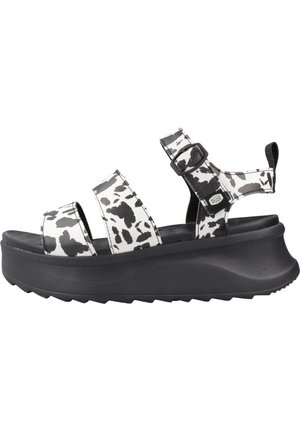 Sandalia de plataforma negra con tiras de estampado de vaca en blanco y negro, hebilla ajustable y puntera abierta, con una lengüeta para tirar en el talón.