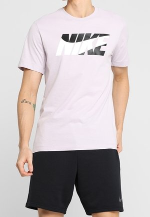 Homme portant un t-shirt à manches courtes rose clair avec un grand texte stylisé en noir et blanc et un short de sport noir.
