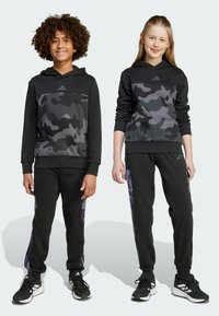 Black hooded sweatshirts with gray camo patterns, paired with black joggers featuring purple side accents. Both are made from soft fabric.