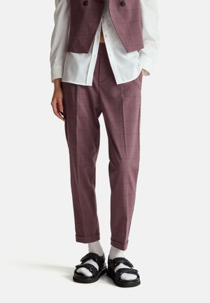 Pantalones de cuadros color burdeos con un corte entallado, combinados con una camisa blanca de cuello y sandalias negras con tiras texturizadas.