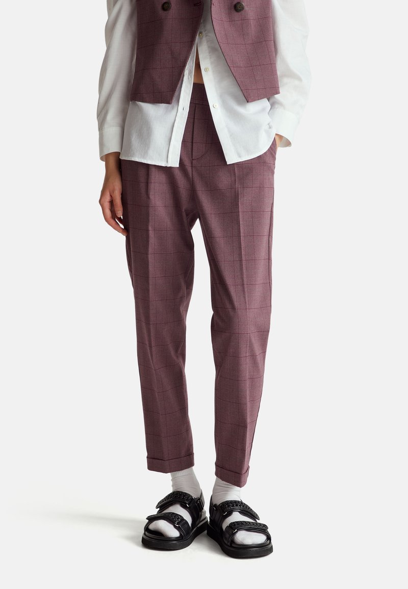 Bordeaux geruite broek met een getailleerde pasvorm, gecombineerd met een witte blouse met kraag en zwarte sandalen met geprofileerde bandjes.