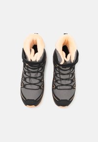 Black and grey high-top athletic shoes with a textured surface, orange accents, and a soft, cream-colored interior lining.