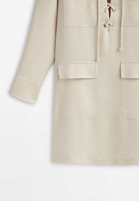 Beige Tunika-Oberteil mit einem geschnürten Ausschnitt, zwei aufgesetzten Fronttaschen, lockerer Passform und langen Ärmeln aus weichem, strukturiertem Stoff.