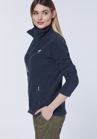 Navy blue fleece jacket with a high collar, zippered pockets, and a soft texture. Features a small logo on the left chest.