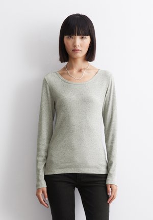 Suéter de manga larga gris claro con textura acanalada, escote en pico y sutiles motas. Combinado con jeans oscuros, diseño minimalista.