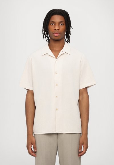 Kortærmet skjorte med knapper i lyst beige stof, tekstureret overflade, fire knapper, notch-krave, lige snit, bæres med lyse bukser.