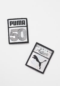 Kaksi suorakaiteen muotoista kangaspalaa, joissa on mustaa, hopeaa ja valkoista väriä. Toinen esittää "PUMA 50" ääriviivoilla, kun taas toisessa on teksti "PANINI Authentic" ja puman siluetti.