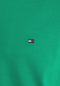 Tissu vert texturé avec un petit logo rectangulaire présentant des blocs horizontaux blancs, rouges et bleu marine au centre.