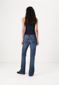 Jean en denim évasé de bleu moyen avec une étiquette marron sur la ceinture arrière. Présente des motifs de couture distincts sur les poches arrière.